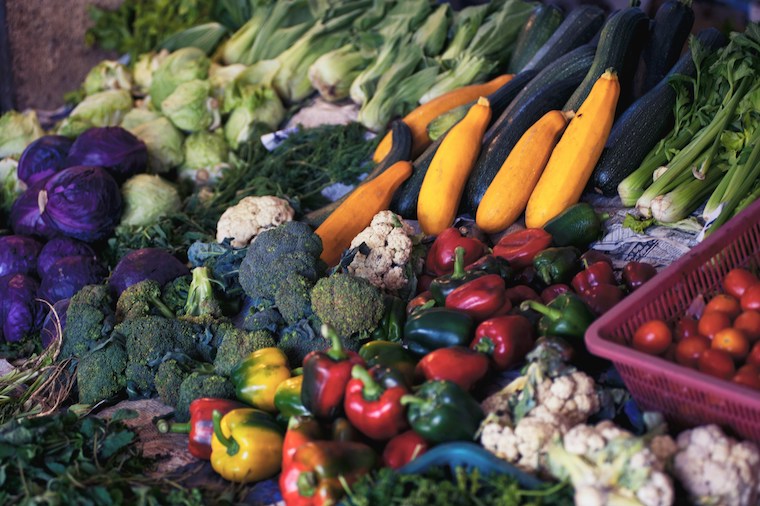 Gemüsesorten wie Brokkoli, Zucchini und Paprika liegen schöln drapiert an einem Marktstand