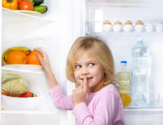 Mädchen vor einem geöffneten Kühlschrank mit Obst und Gemüse