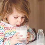 Kleines Mädchen trinkt ein Glas Milch.