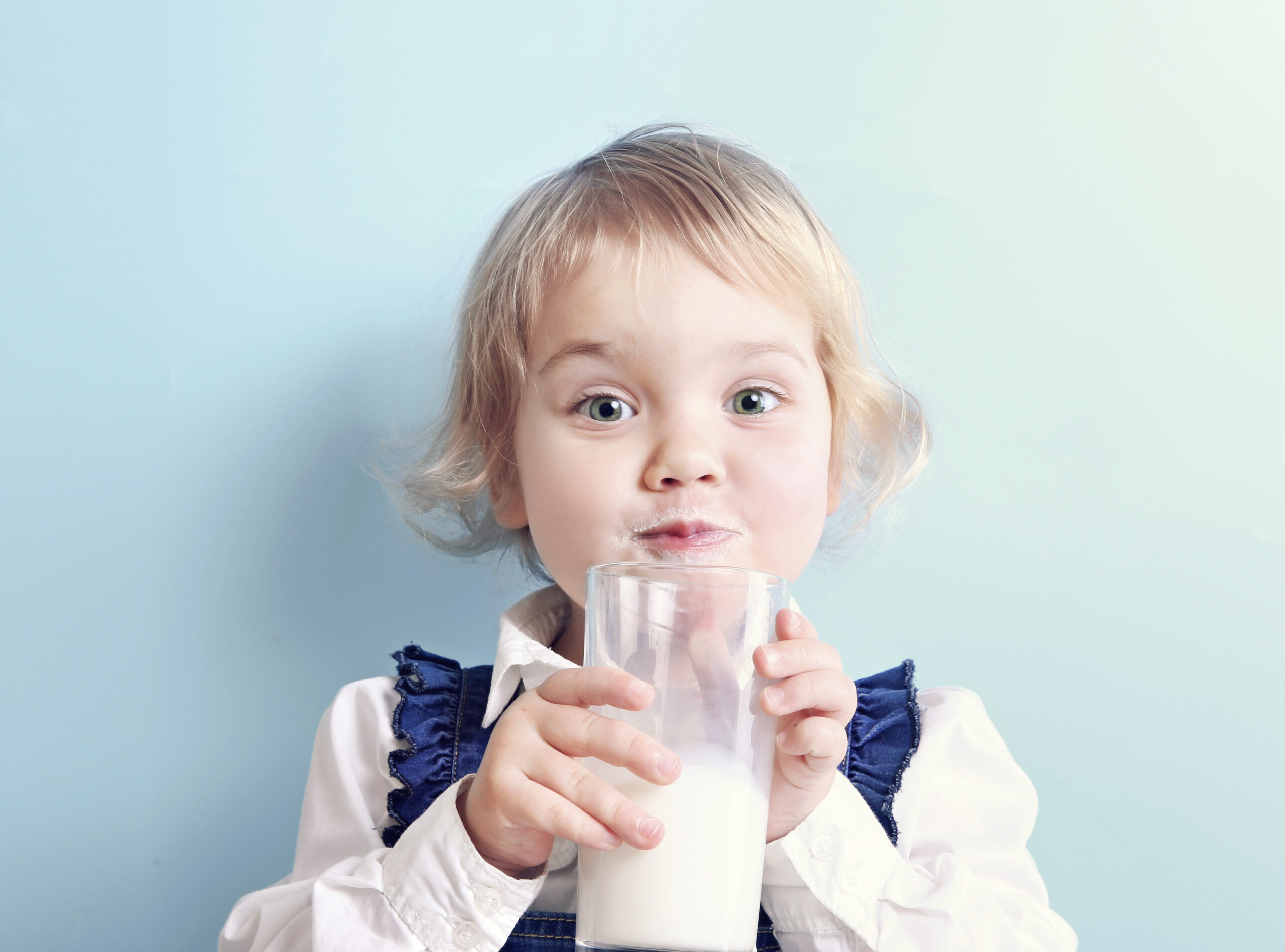 Ein Kleinkind mit blondem Haar trinkt Milch oder eine Milchalternative aus einem Glas